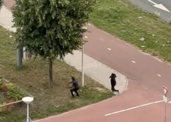Twee mannen met capuchons gooien stenen naar man die flesjes en blikjes aan het verzamelen