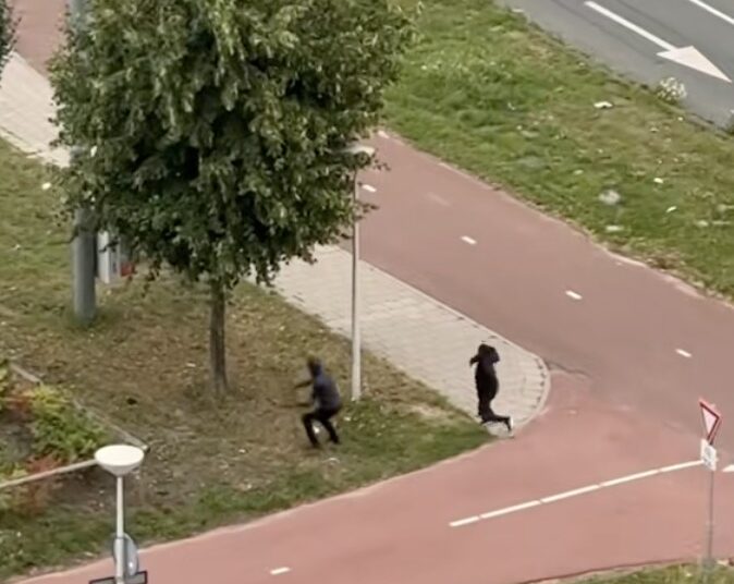 Twee mannen met capuchons gooien stenen naar man die flesjes en blikjes aan het verzamelen