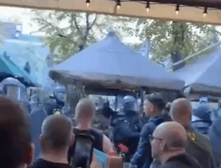 ME lopen langs een terras en spuiten pepperspray richting mensen.